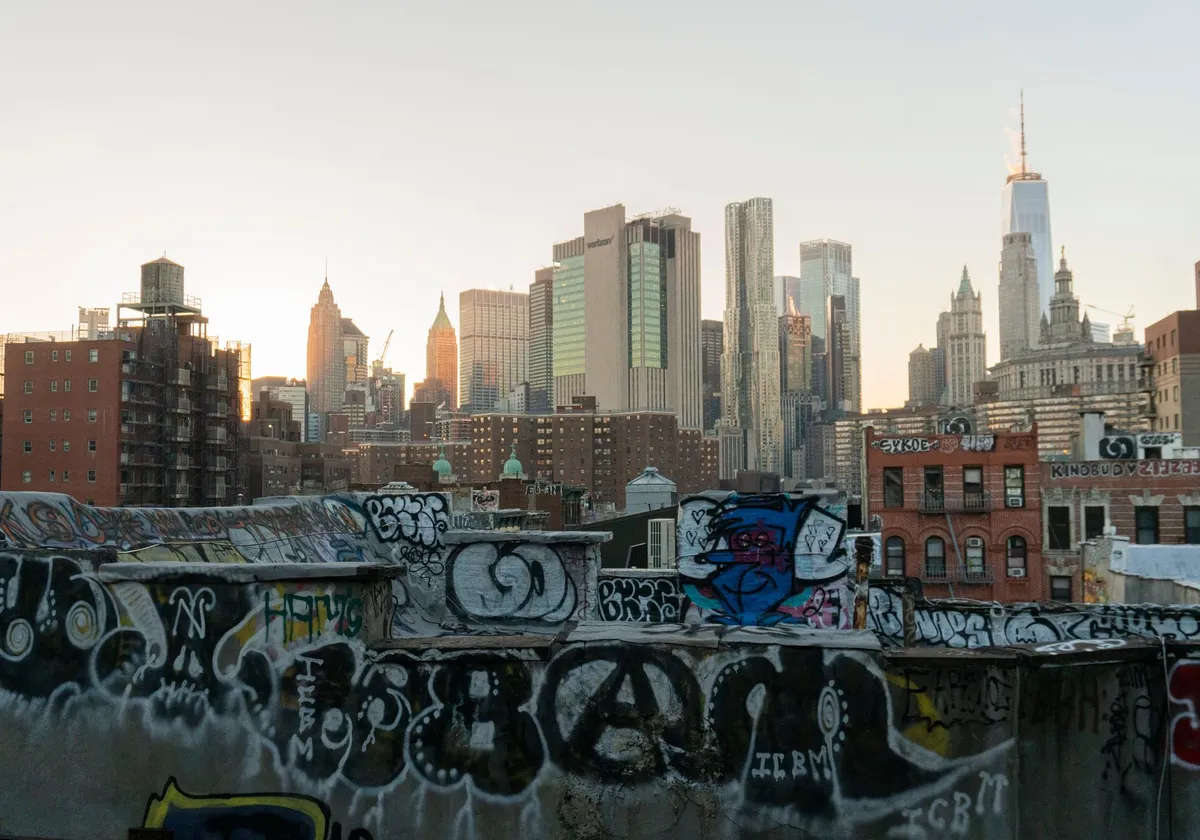 View of New York City skyline from a graffiti-covered rooftop at sunset.